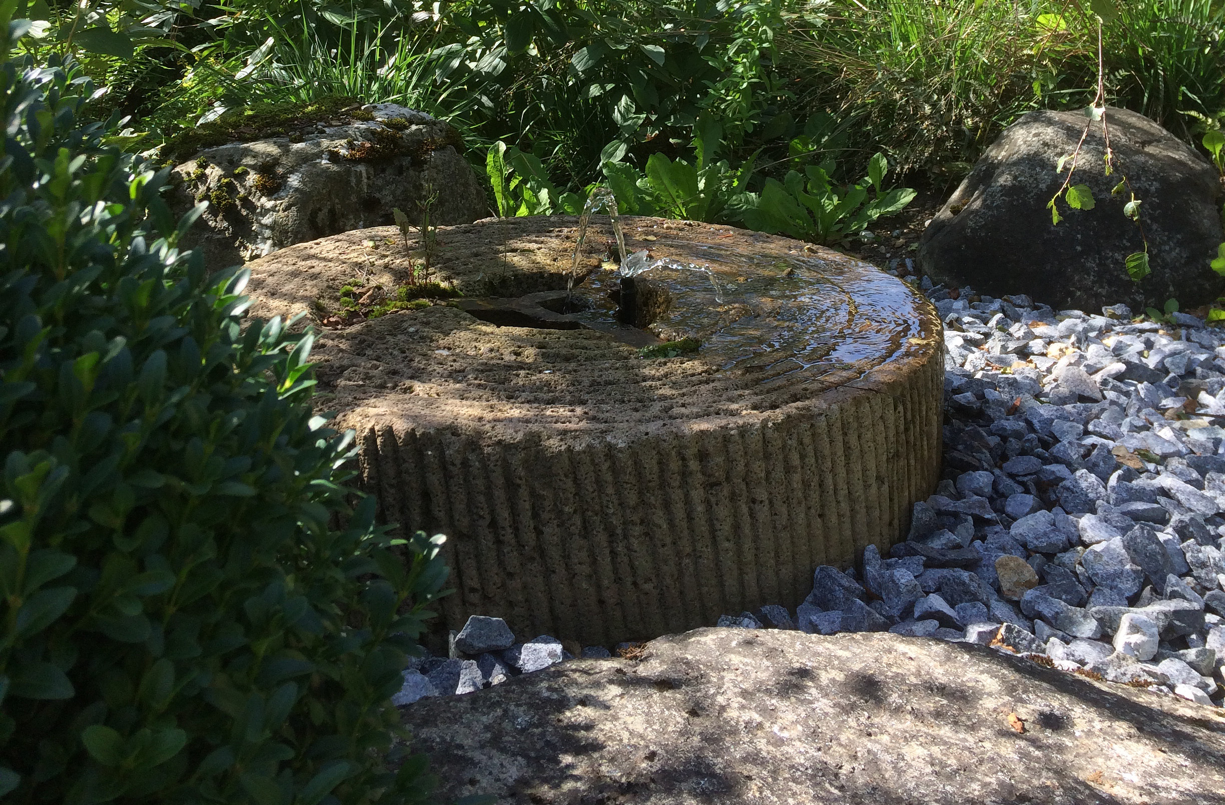 Sprudelndes Wasser auf einem Mühlstein im Quellraum des Landgartens