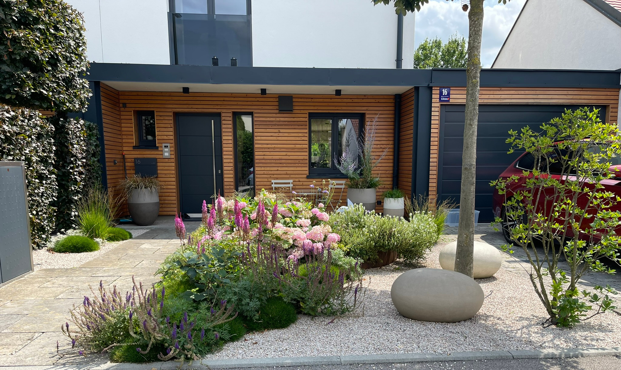 Vorgarten mit blütenreicher Pflanzung, Atelier-Vierkant-Gefäßen und skulpturalen Natursteinen