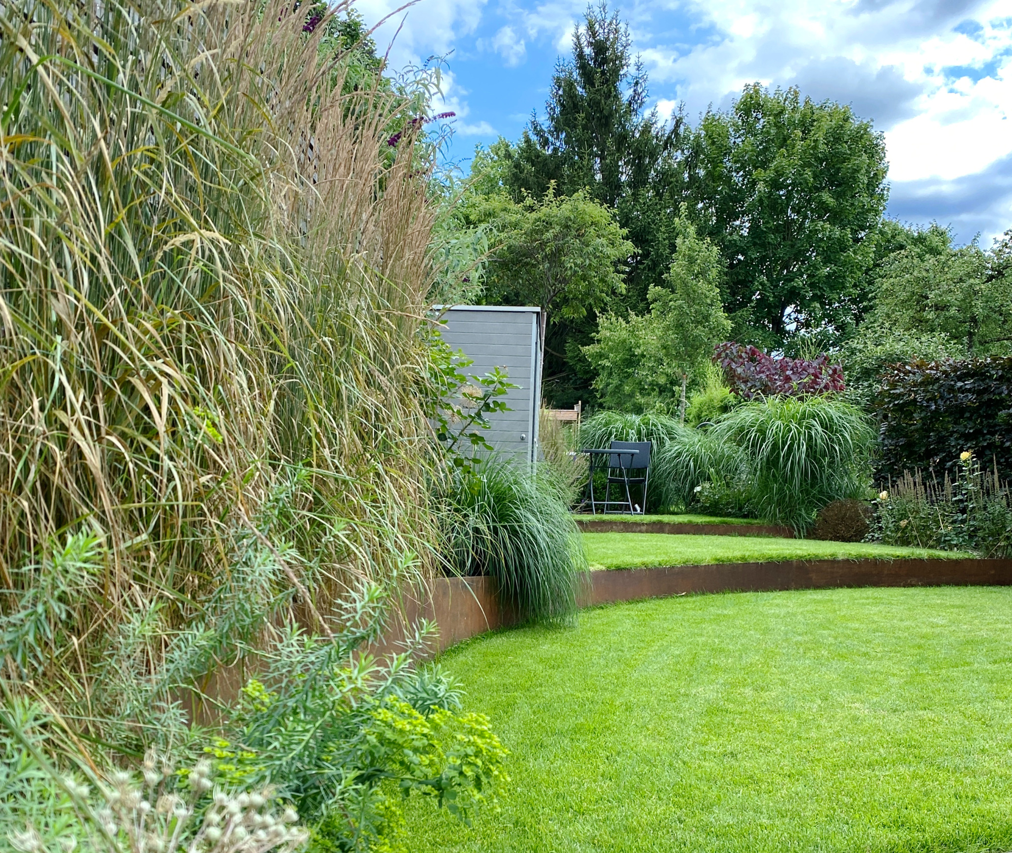 Geschwungene Cortenstahlbänder vergrößern räumlich den schmalen Garten Karwath